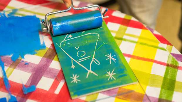 Eine blau-grün gefärbte Linolplatte. Jemand fährt mit einer blauen Farbwalze darüber.