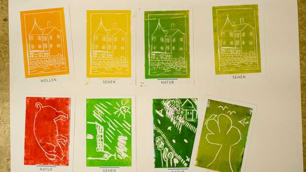 Eine Reihe bunt bedruckter Postkarten in den Farben rot, hellgrün, dunkelgrün, gelb und orange.