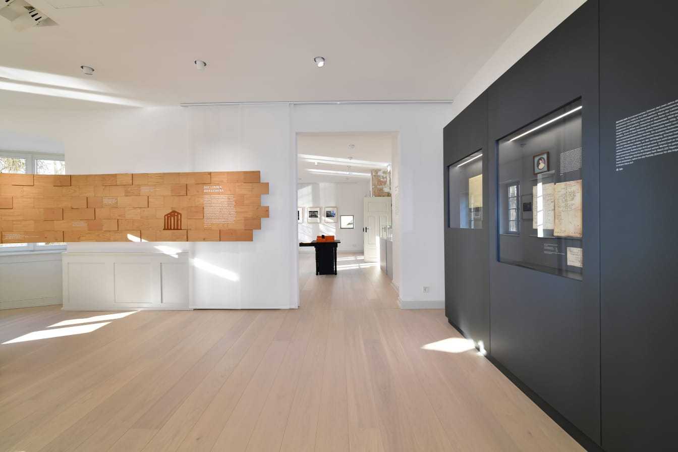 Bild des ersten Raumes der Dauerausstellung: Das Gedicht ›Die Linien des Lebens…‹ auf Holzschindeln und eine graue Vitrine mit Dokumenten