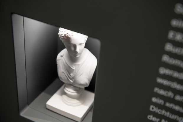 Eine kleine weiße Figur von einer Frau. Die feinen Lockenhaare sind zu einem Zopf hochgesteckt.