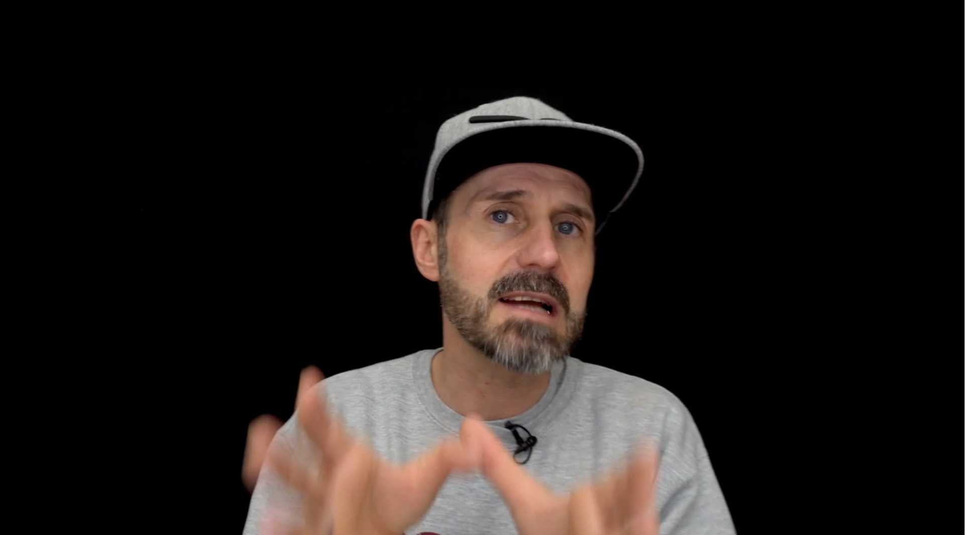 Der Rapper Spax trägt einen grauen Pullover und eine graue Baseball-Cap.