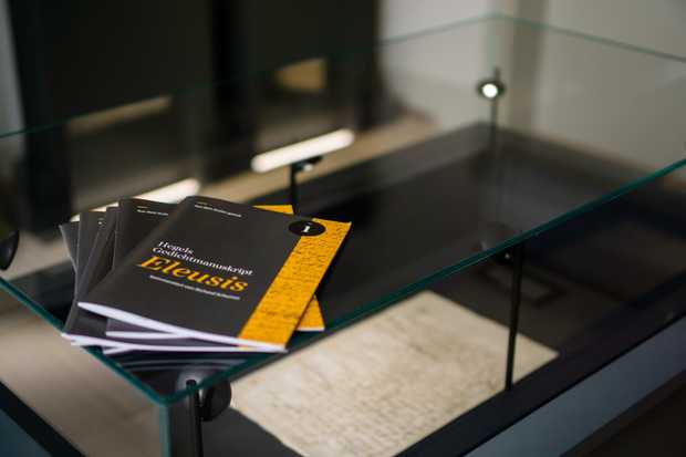 Eine Vitrine mit einem Manuskript. Darauf liegen dunkelgraue Hefte mit gelbem Rand und Titel.