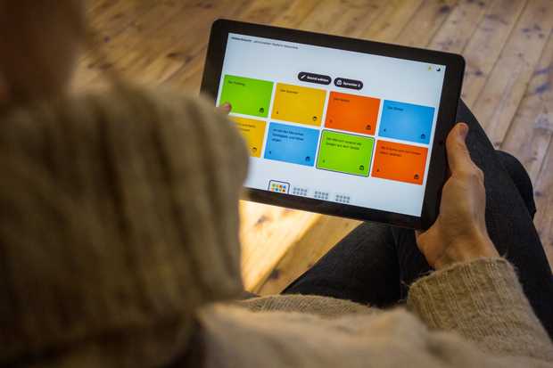 Auf einem Tablet sind bunte Kacheln in den Farben blau, grün, orange und gelb zu sehen. Eine Person wählt daraus die grüne Kachel mit der Aufschrift ›Der Frühling‹ aus.