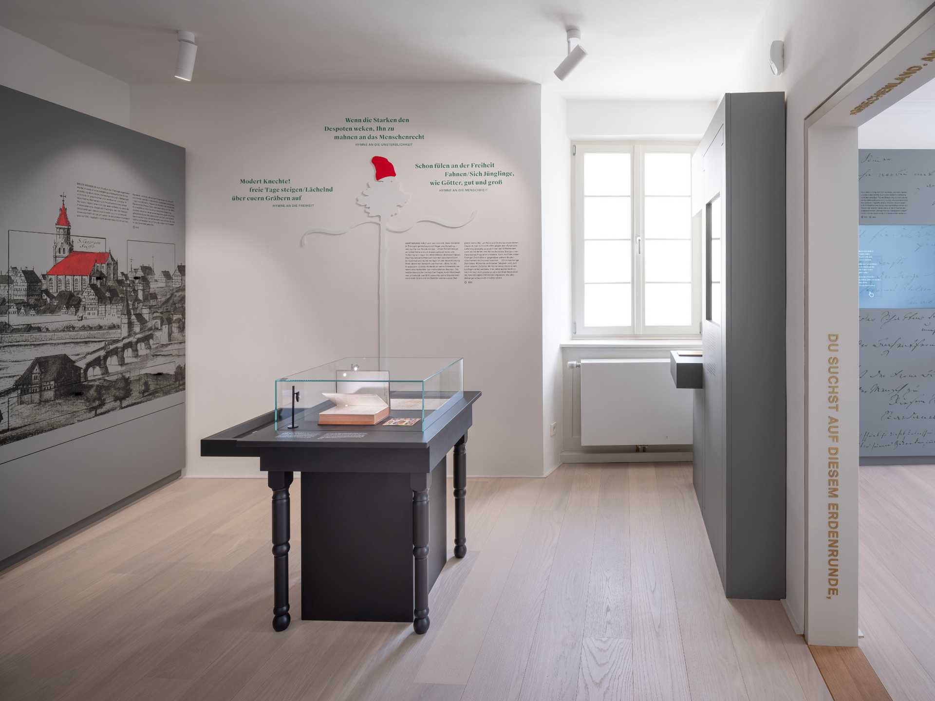 Bild des Raumes Tübinger Hoffnungen im ersten Stock des Turms. An der Wand Zitate und ein Freiheitsbaum, an der linken Wand eine graue Vitrine mit historischer Stadtansicht