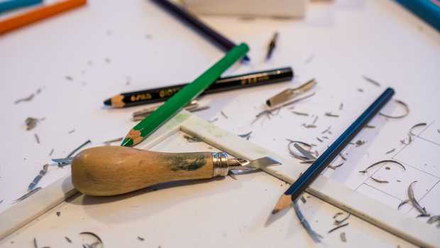 Auf weißen Arbeitsplatten liegen ein Linolschnitt-Werkzeug und einige Buntstifte.
