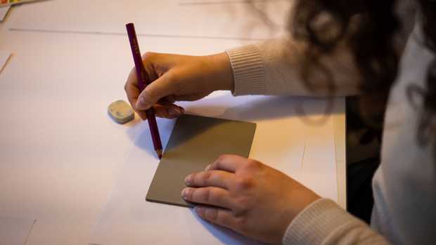 Jemand zeichnet den Umriss einer Linolplatte auf ein Papier.