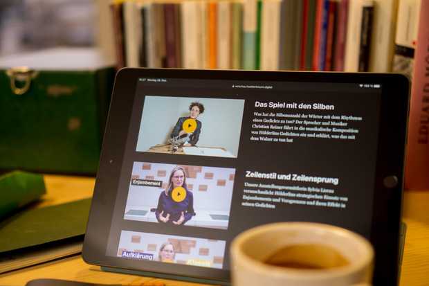 Auf einem Tisch vor einer Bücherwand steht ein Tablet. Darauf sind Videos aus dem Turm-TV zu sehen.