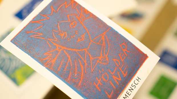 Eine Postkarte mit orange leuchtenden Linien und Hintergrund. Darüber ist mit blauer Farbe eine zweite Schicht gedruckt.