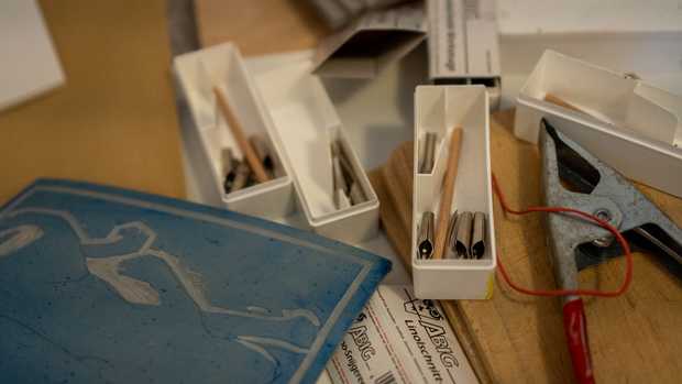 Eine Holzplatte mit Linol-Bestecken, einer blauen Linolplatte und einer Klemmzange.